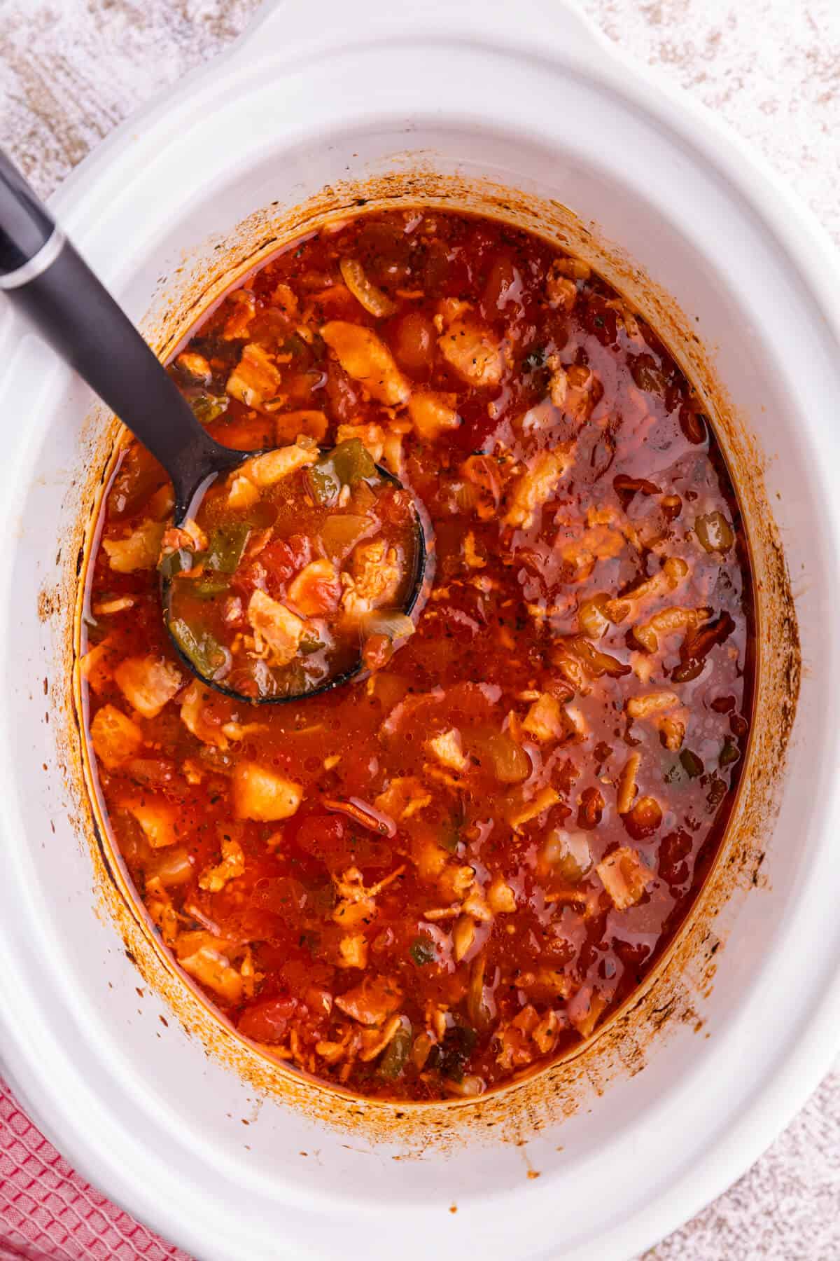 Pizza soup in a white slow cooker with a ladle.