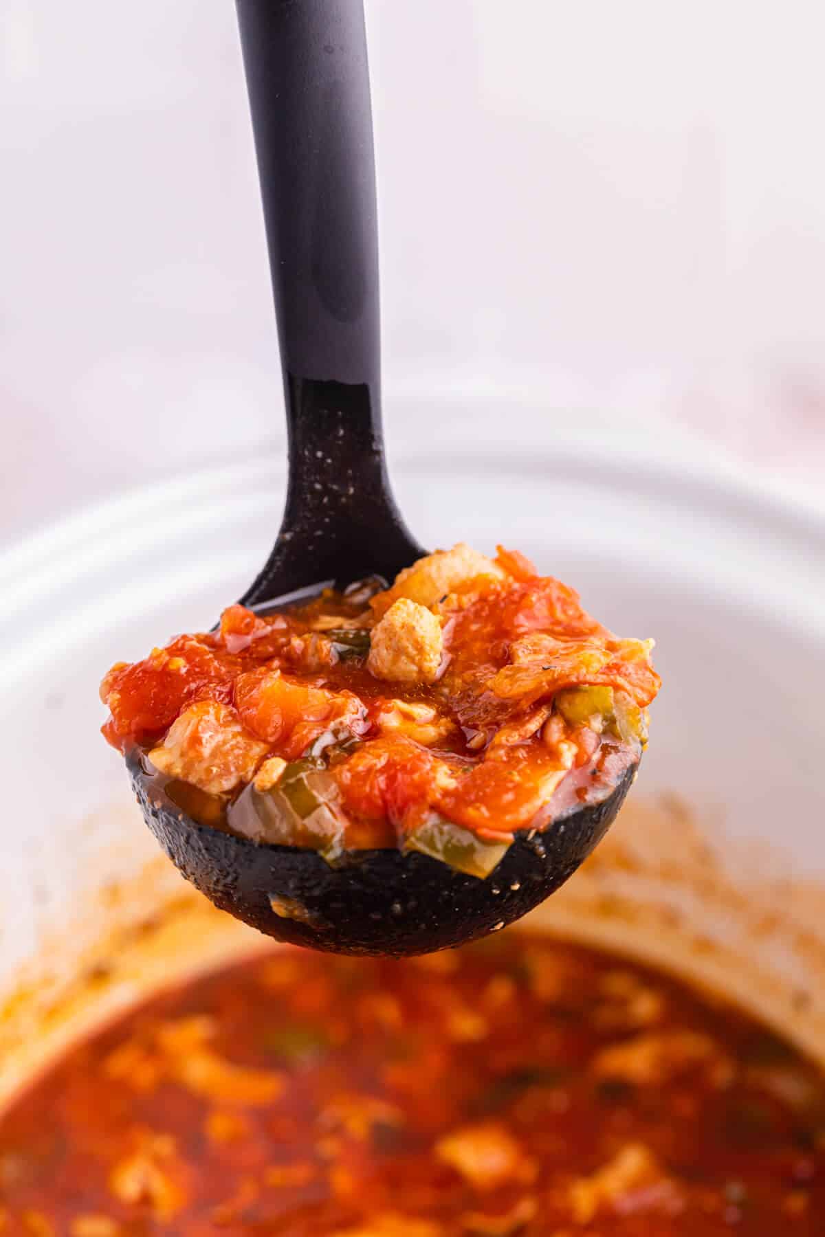 Pizza soup in a ladle over a slow cooker.