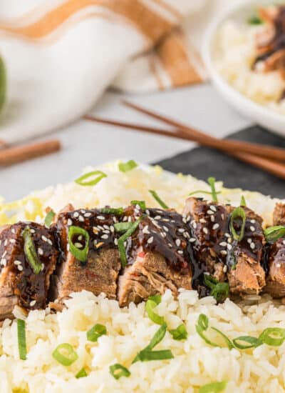 Sliced Asian pork tenderloin on a bed of rice and cabbage.