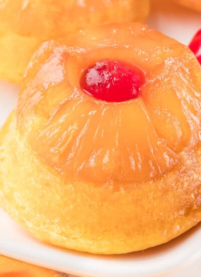 A pineapple upside down cupcake on a platter with cherries.
