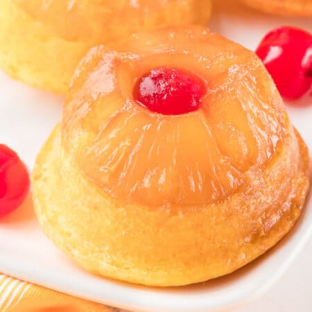 A pineapple upside down cupcake on a platter with cherries.