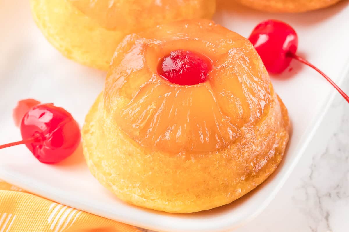 A pineapple upside down cupcake on a platter with cherries.