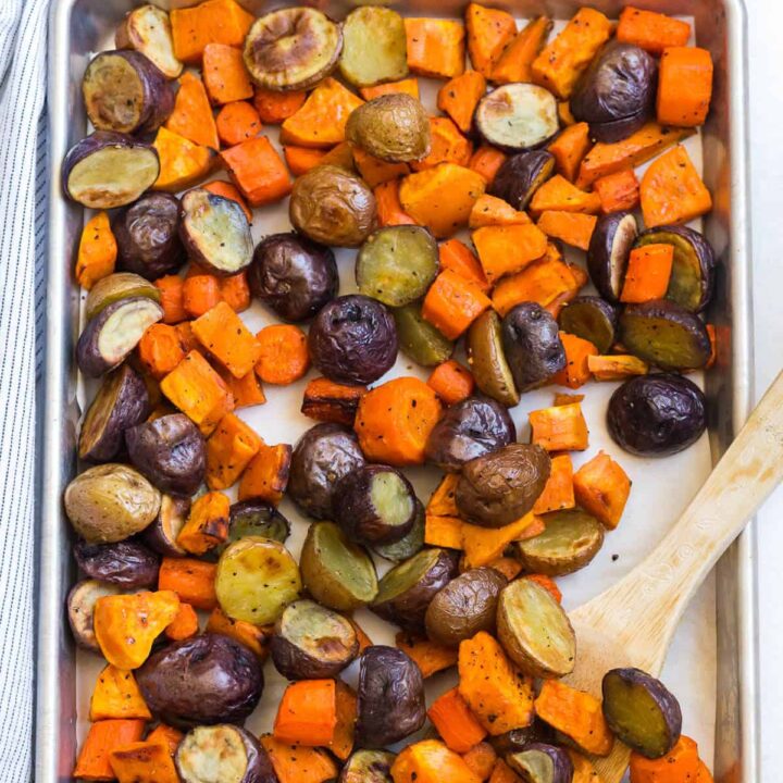 Roasted root vegetables on a sheet pan with a wooden spoon.