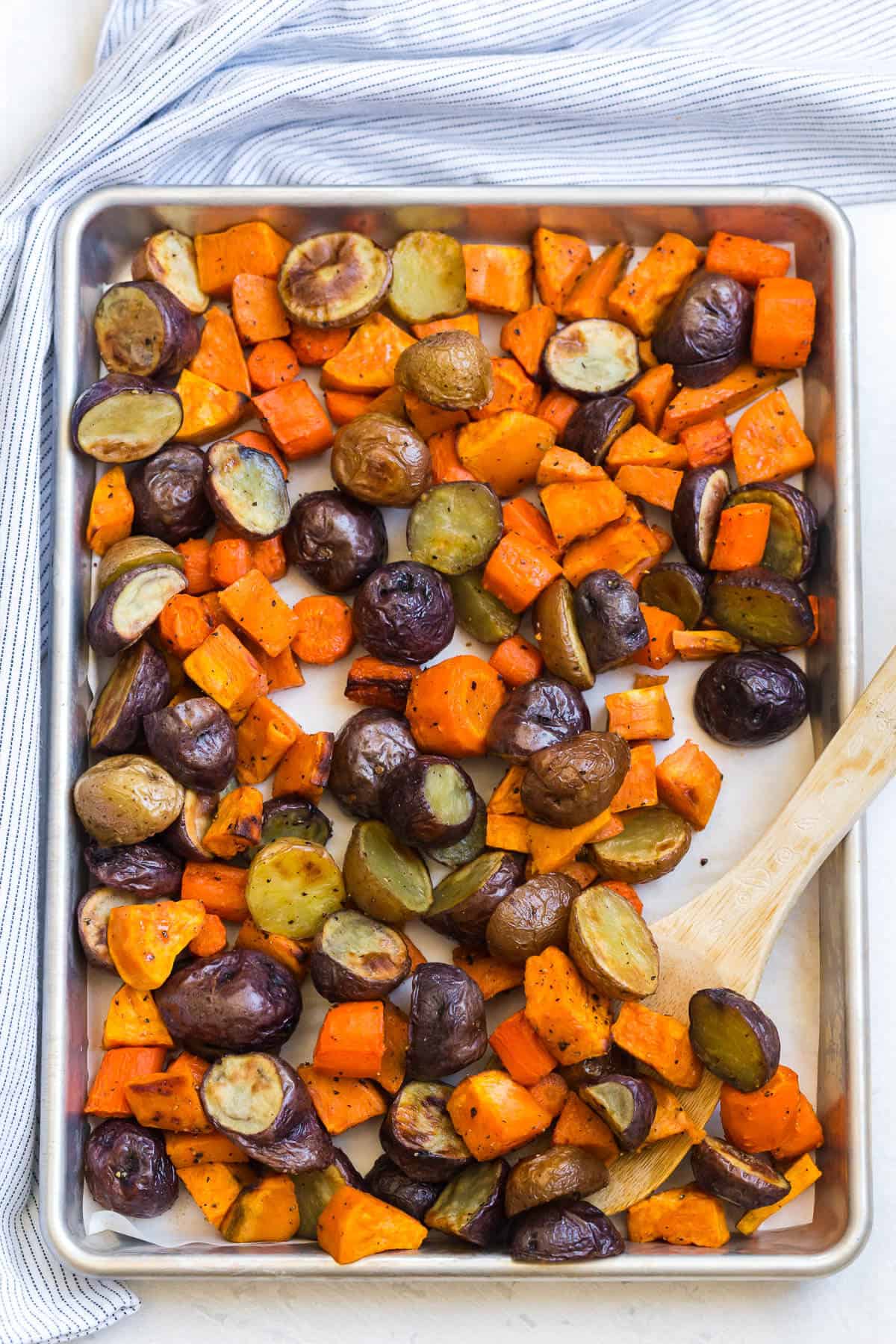 Roasted root vegetables on a sheet pan with a wooden spoon.