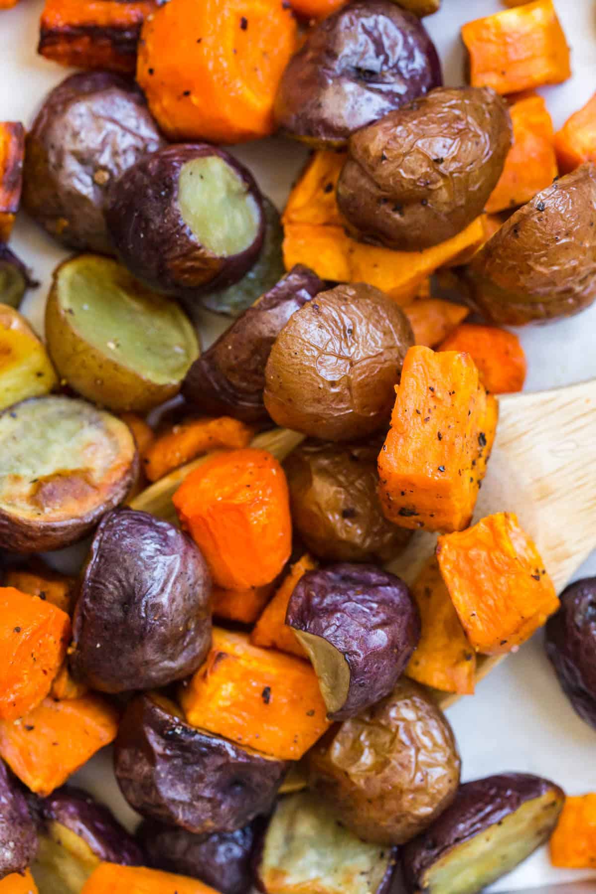 Roasted root vegetables on a sheet pan with a wooden serving spoon.