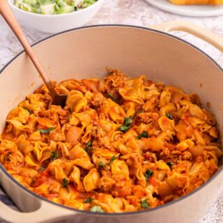 A dutch oven of sausage and cheese cappelletti with a serving spoon.