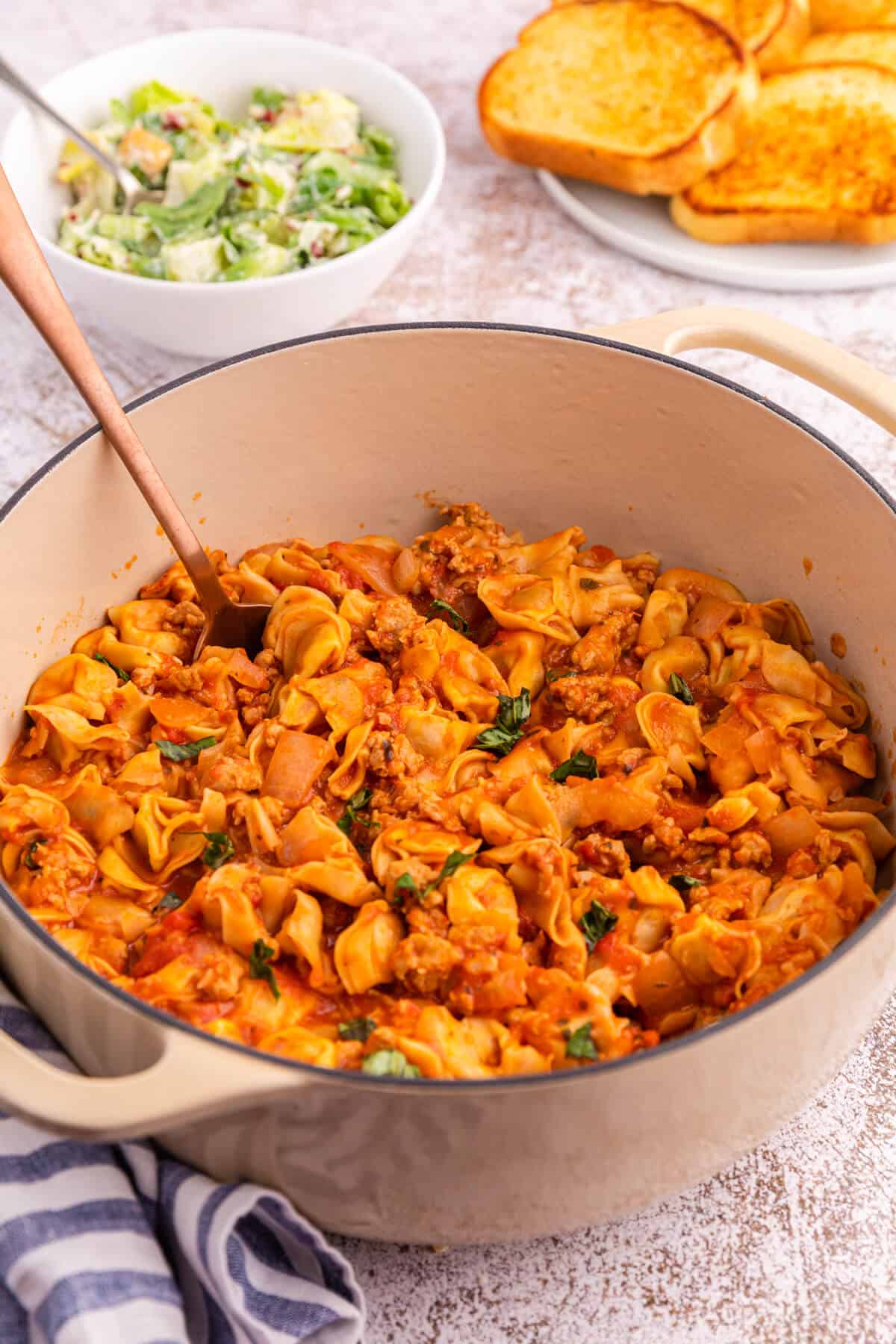 A dutch oven of sausage and cheese cappelletti with a serving spoon.