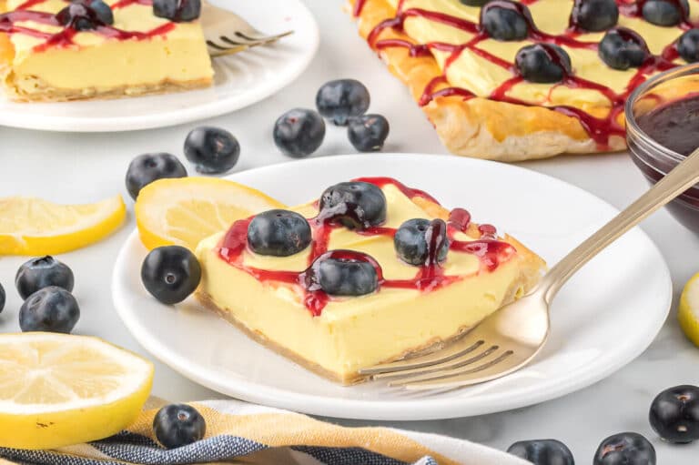 A slice of blueberry lemon tart on a plate with a fork.