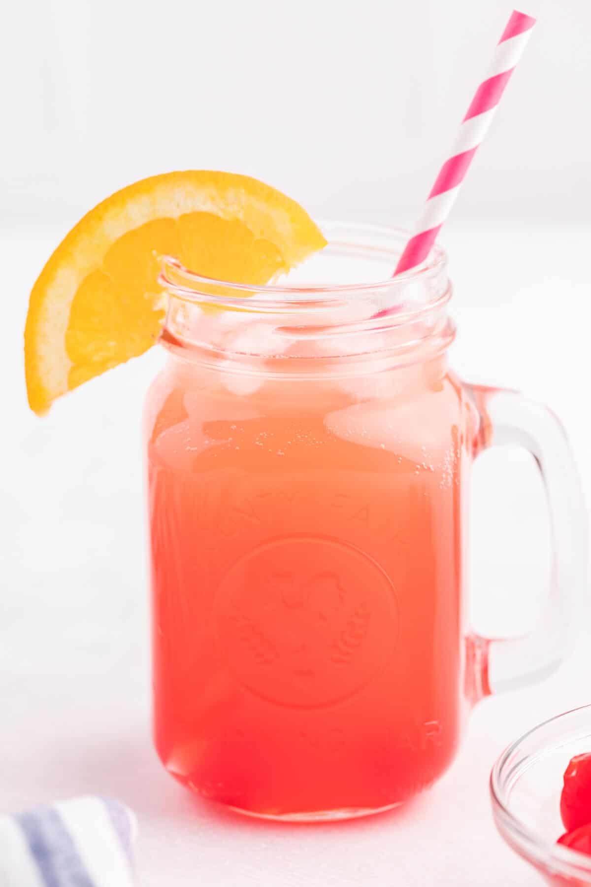 A shirley temple drink in a glass mug with a straw and an orange slice for garnish.