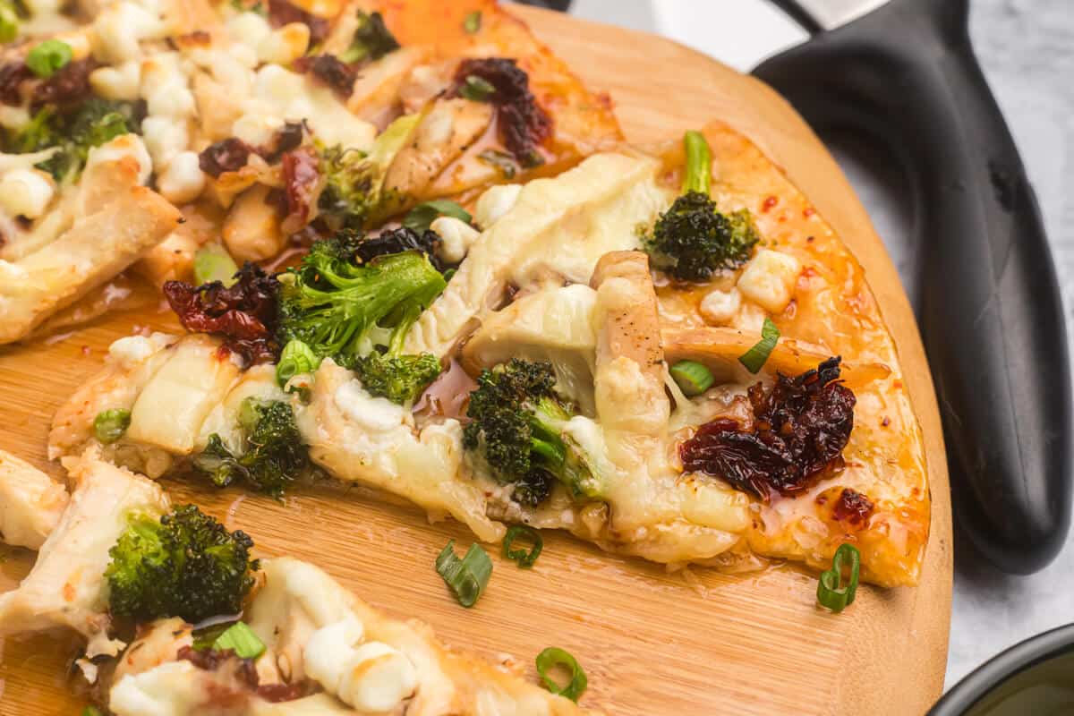 Slices of sweet chili chicken thai pizza on a wooden cutting board.