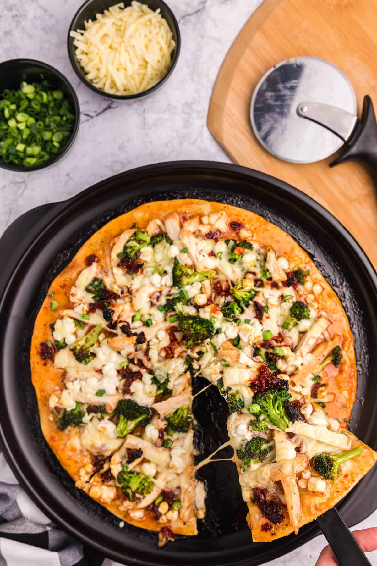 A sweet chili chicken thai pizza with a slice cut and being lifted out of the pan.