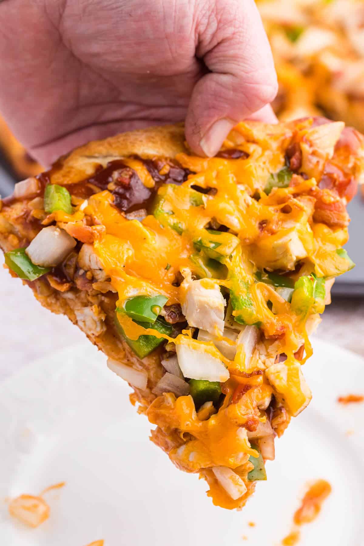 A hand holding a slice of BBQ Chicken Pizza.