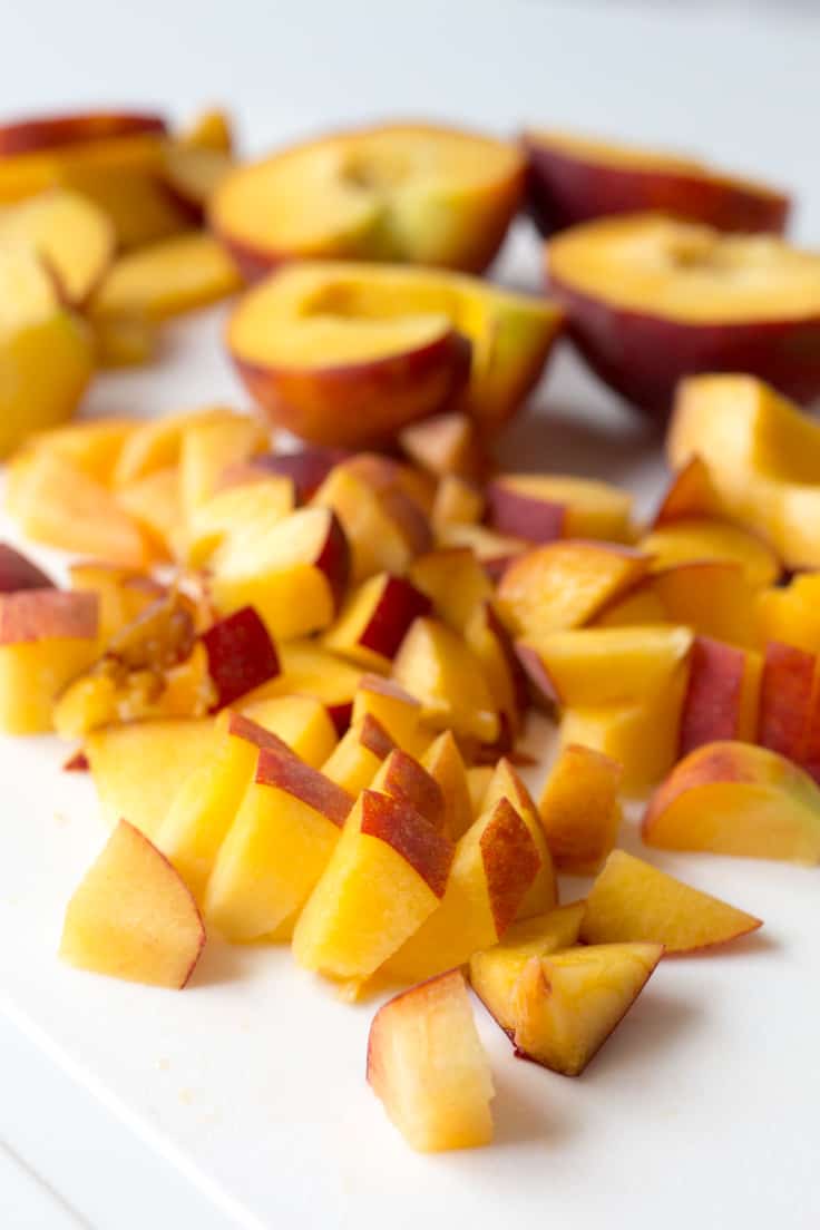 Cut peaches on a white cutting board.