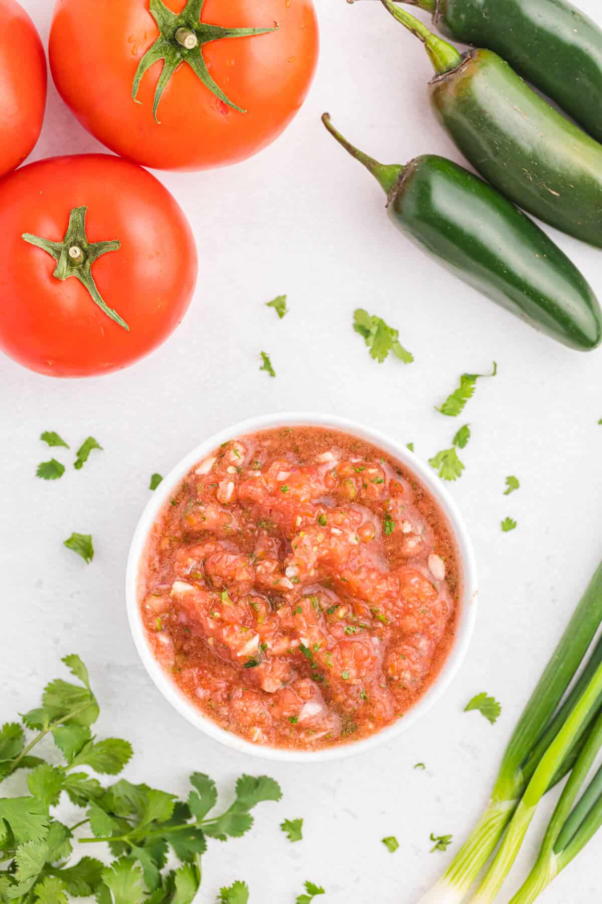 Garden salsa in a bowl surrounded by the ingredients to make it.