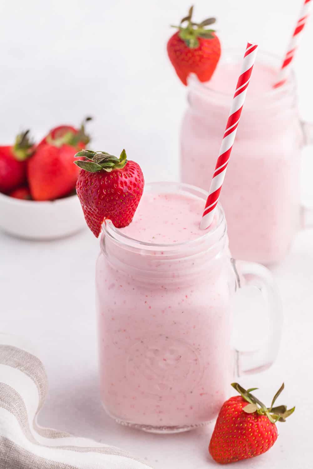Strawberry vanilla smoothie in a glass mug with a straw and strawberry garnish.