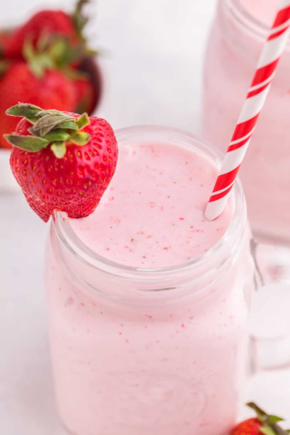 Strawberry vanilla smoothie in a glass mug with a straw and strawberry garnish.