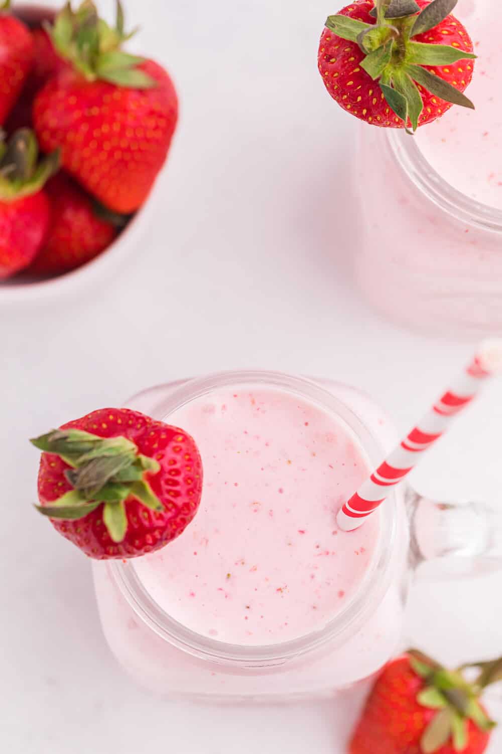 Strawberry vanilla smoothie in a glass mug with a straw and strawberry garnish.