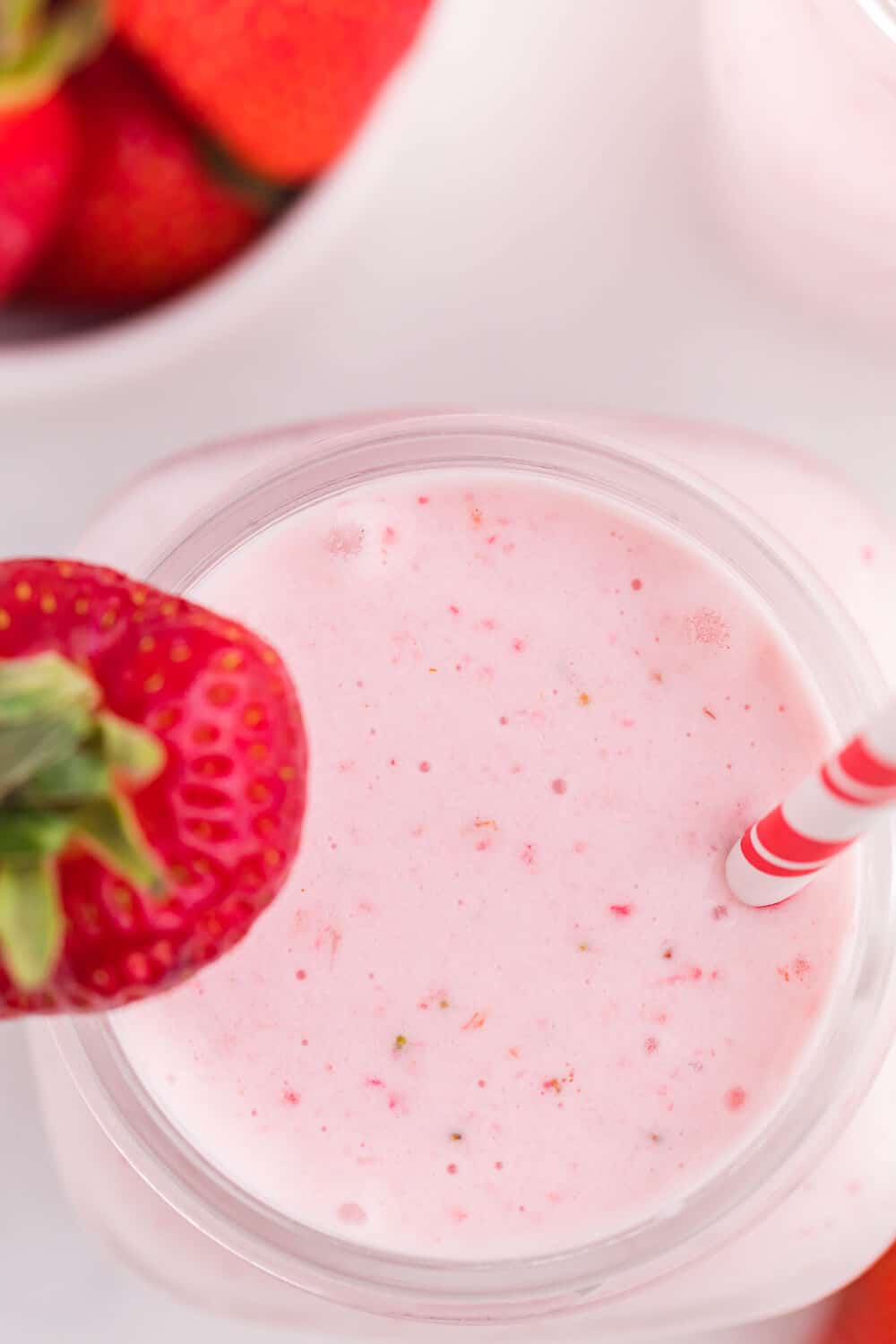 Strawberry vanilla smoothie in a glass mug with a straw and strawberry garnish.