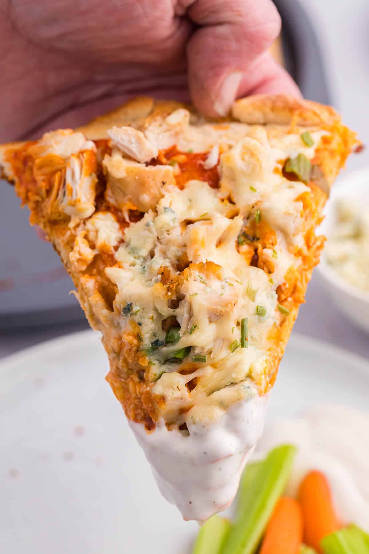 A hand holding a buffalo chicken pizza with ranch dipped on the tip.