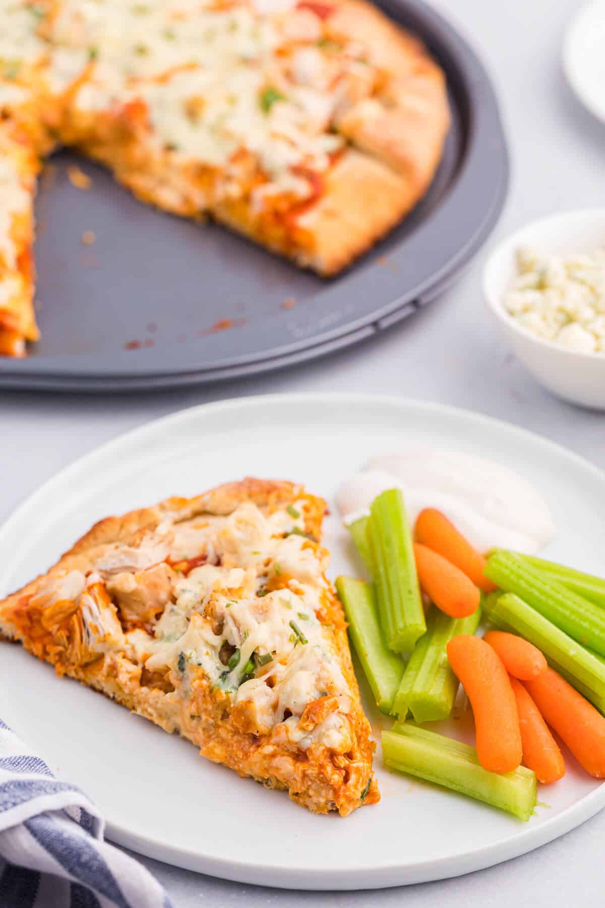 A slice of buffalo chicken pizza on a plate with carrots and celery sticks.