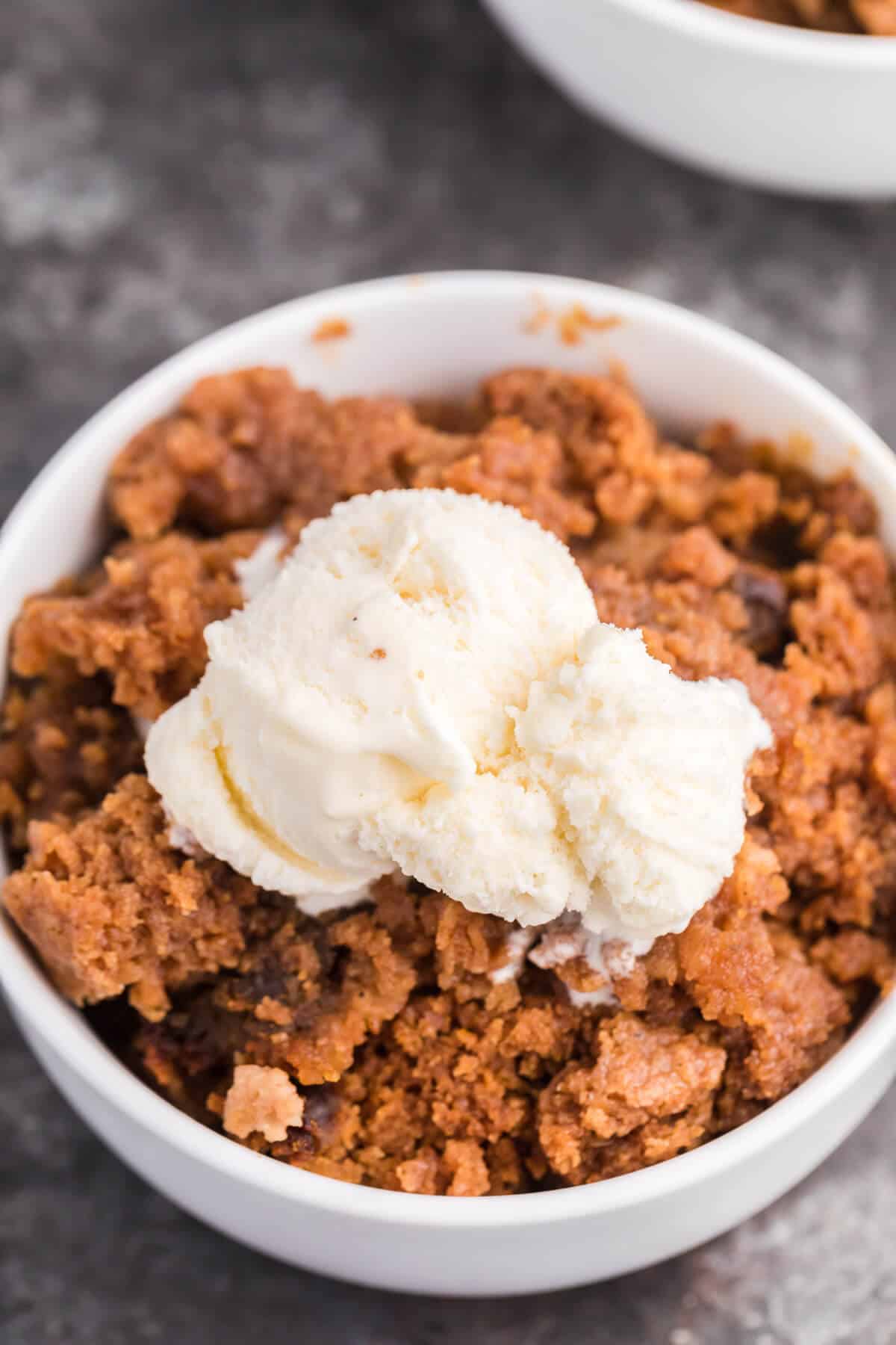 close up of pumpkin dump cake in a bowl topped with vanilla ice cream