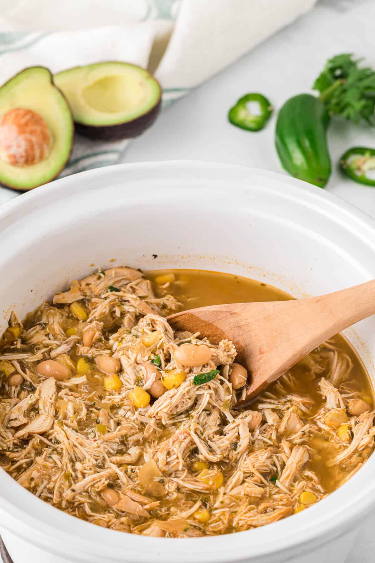 Verde Chicken Chili in a white slow cooker with a wooden spoon.