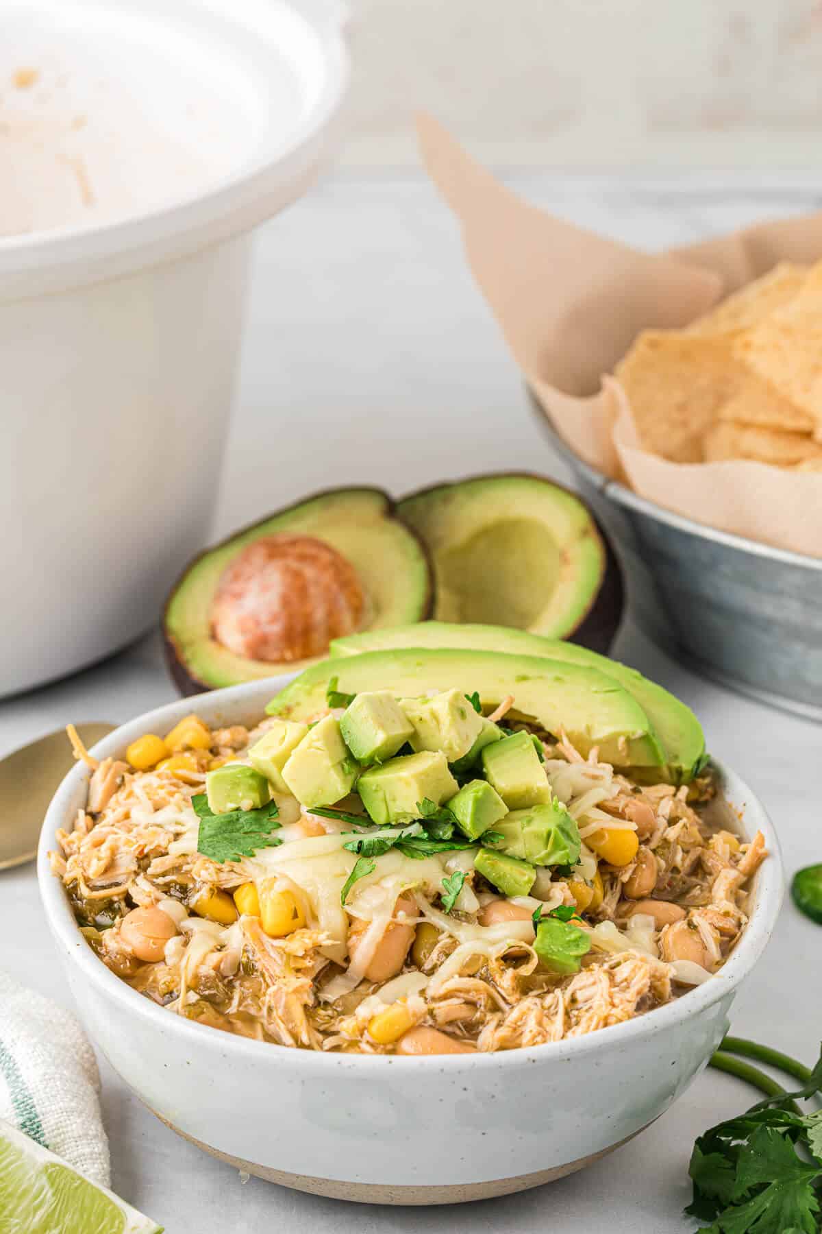 Slow cooker verde chicken chili in a white bowl topped with avocado.