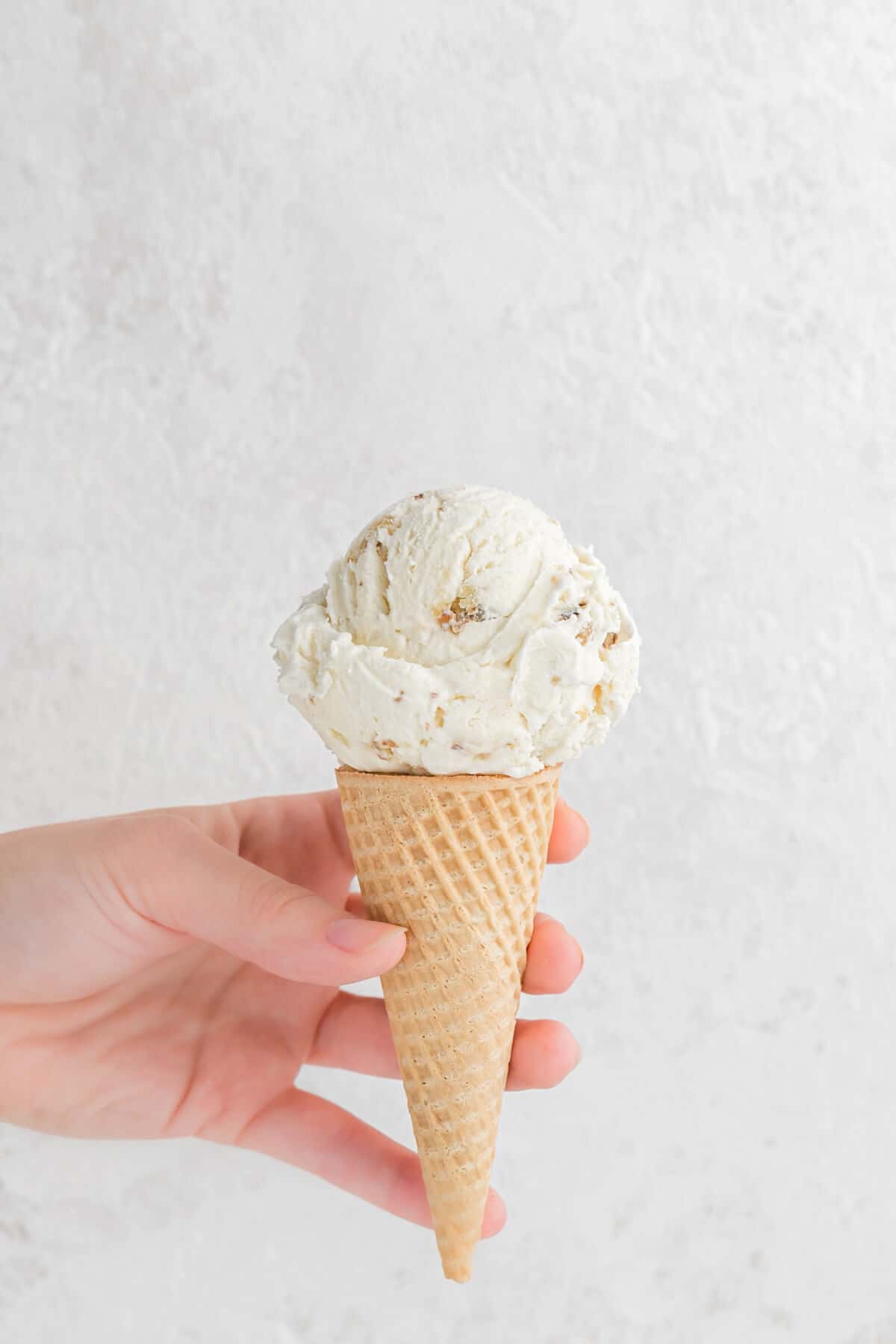 A hand holding a maple walnut ice cream cone.
