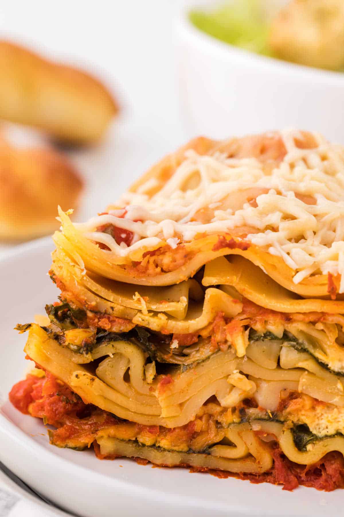 A piece of lasagna on a plate showing the layers.