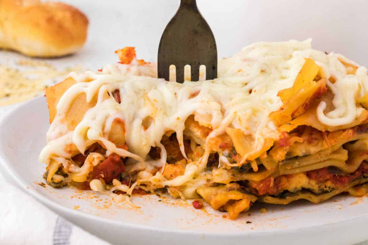 A piece of lasagna on a plate with a fork in it.