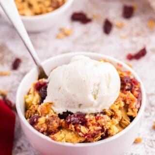 Cranberry cobbler dump cake with vanilla ice cream on top in a bowl.