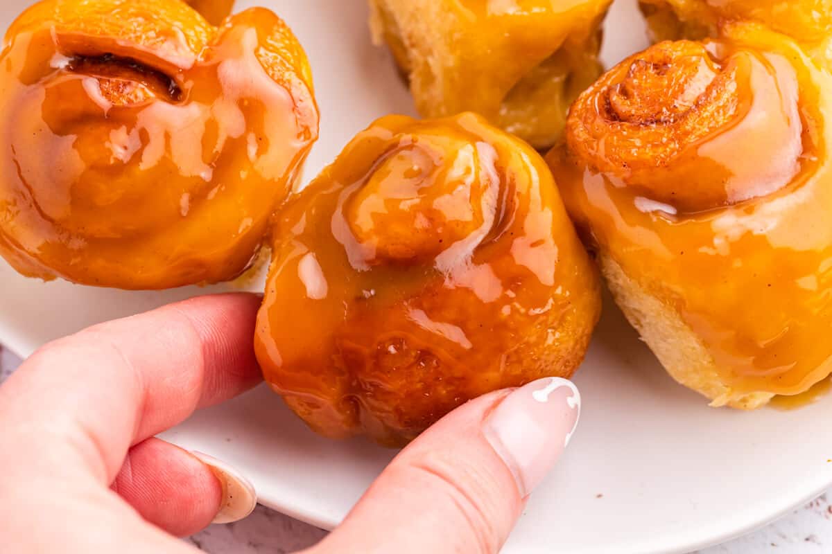 A hand holding a mini rum butter cinnamon roll.