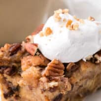 A slice of cinnamon raisin bread pudding on a plate topped with whipped cream.