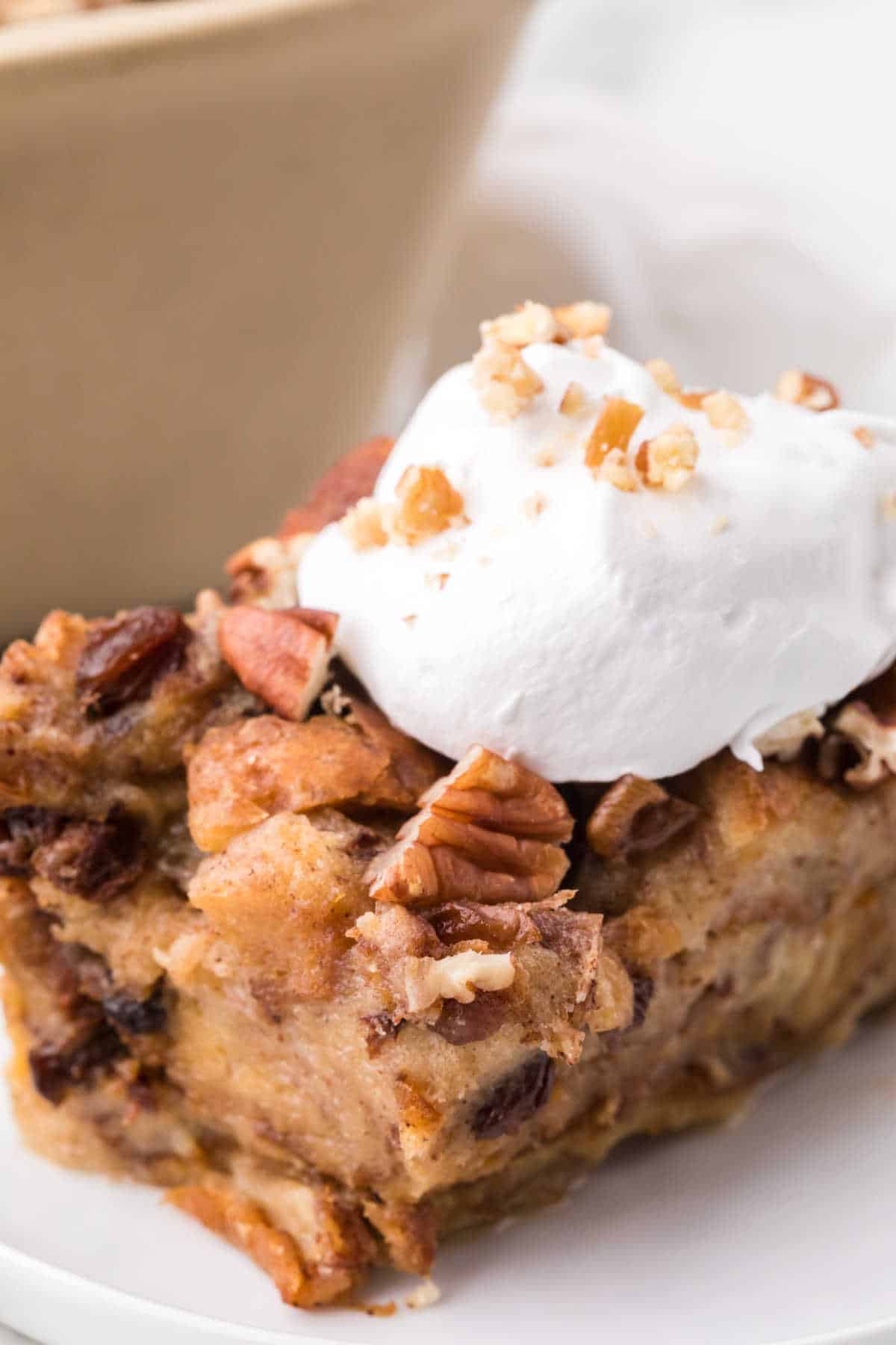 A slice of cinnamon raisin bread pudding on a plate topped with whipped cream.