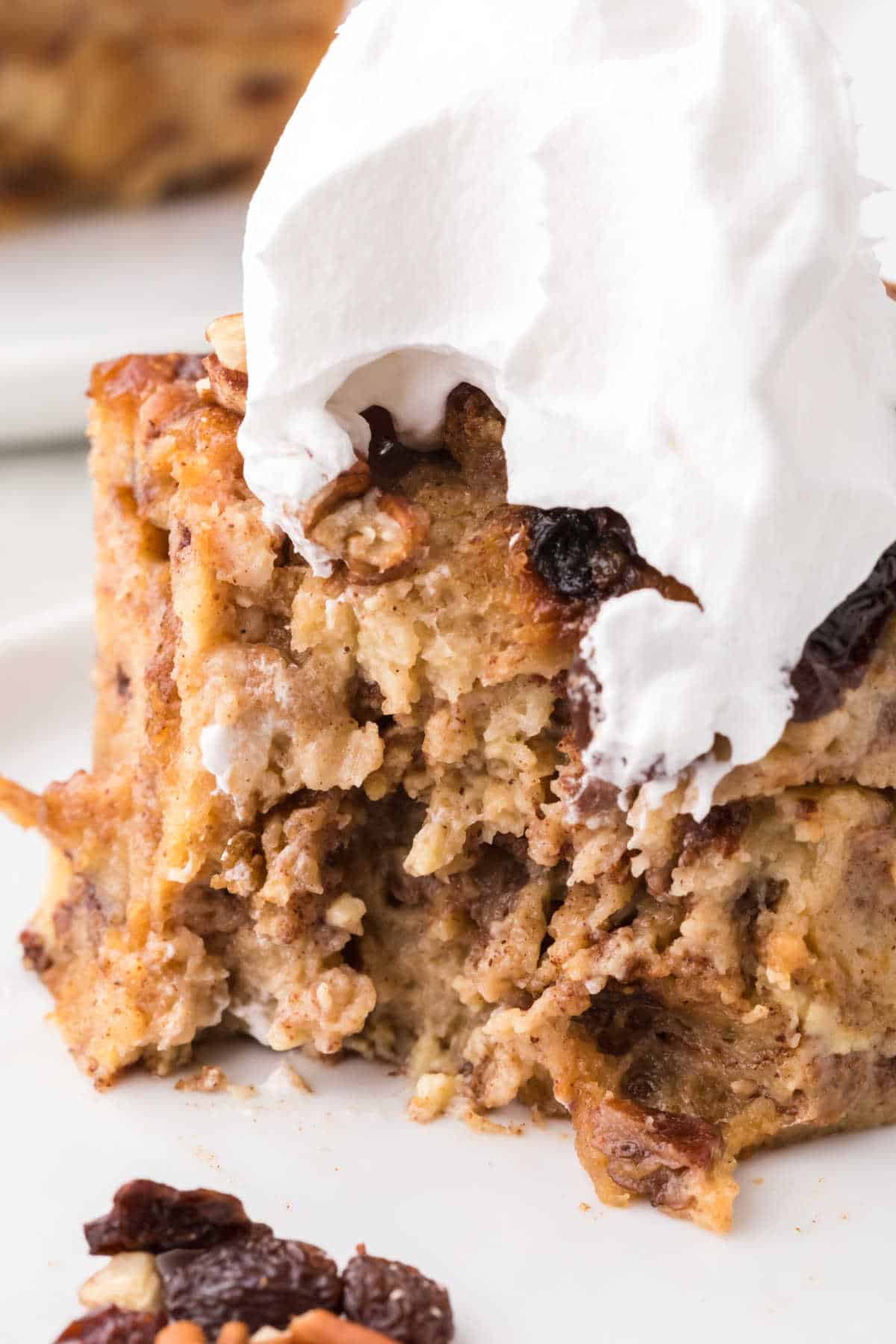 A cinnamon raisin bread pudding slice with whipped cream on a plate.