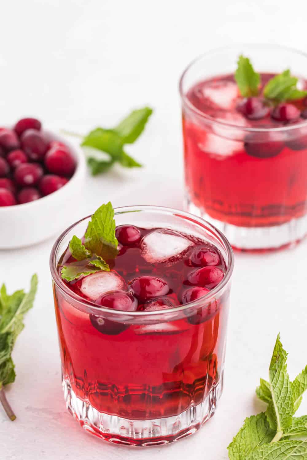 Glasses of cranberry mint mocktail on a white surface.