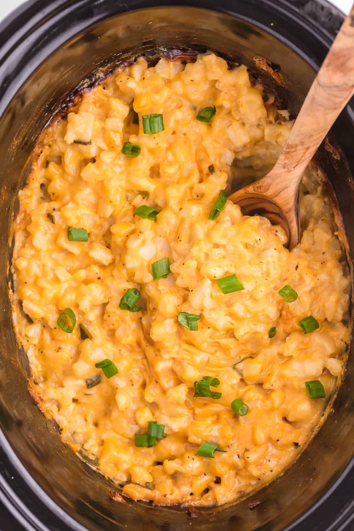 Cheesy potatoes up close in a crockpot with a serving spoon