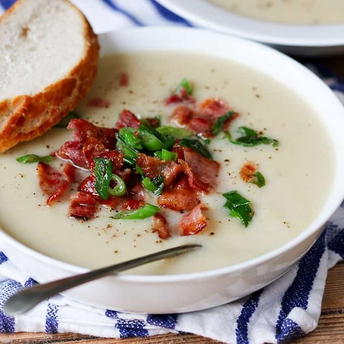 A bowl of cauliflower soup with a slice of bread with a spoon.