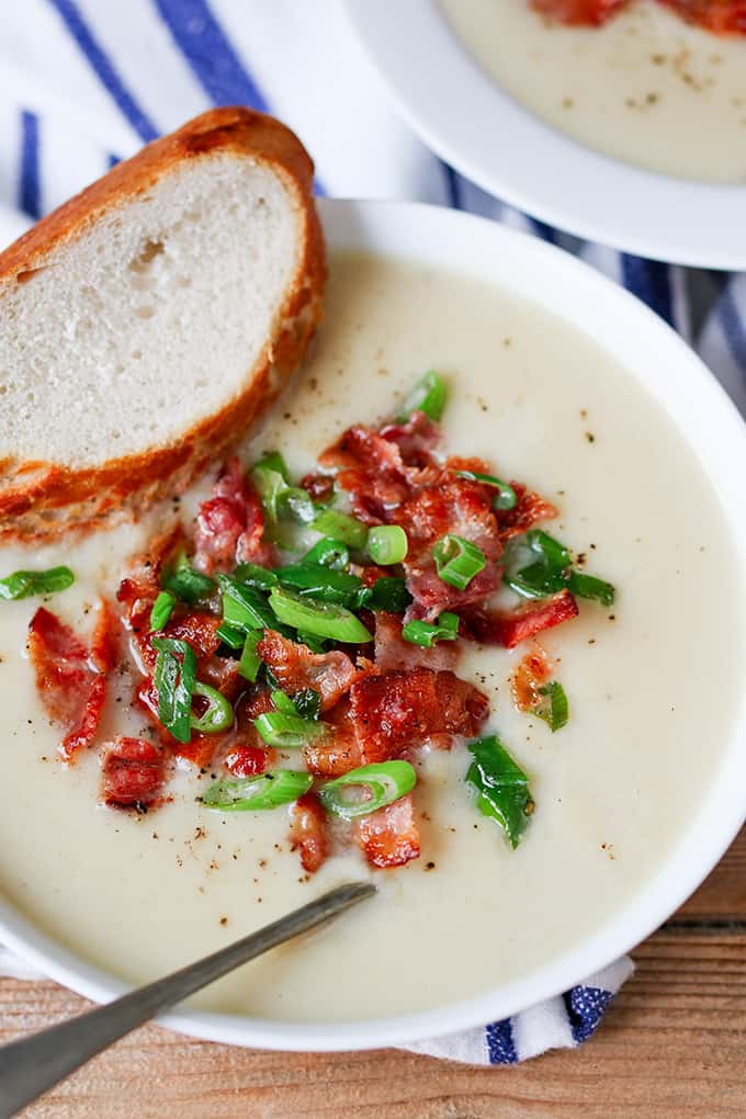 Cauliflower soup with bacon in a bowl with a spoon and a slice of bread.