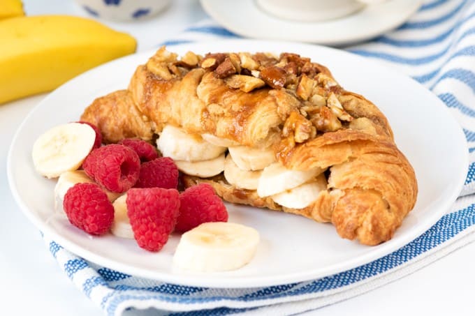 Sticky banana croissant on a white plate with bananas and raspberries.