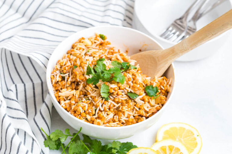 Curried lentil rice in a white bowl with a wooden spoon.