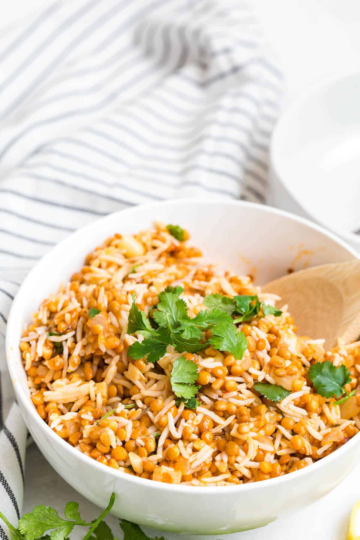 Curried lentil rice in a bowl with a wooden spoon.