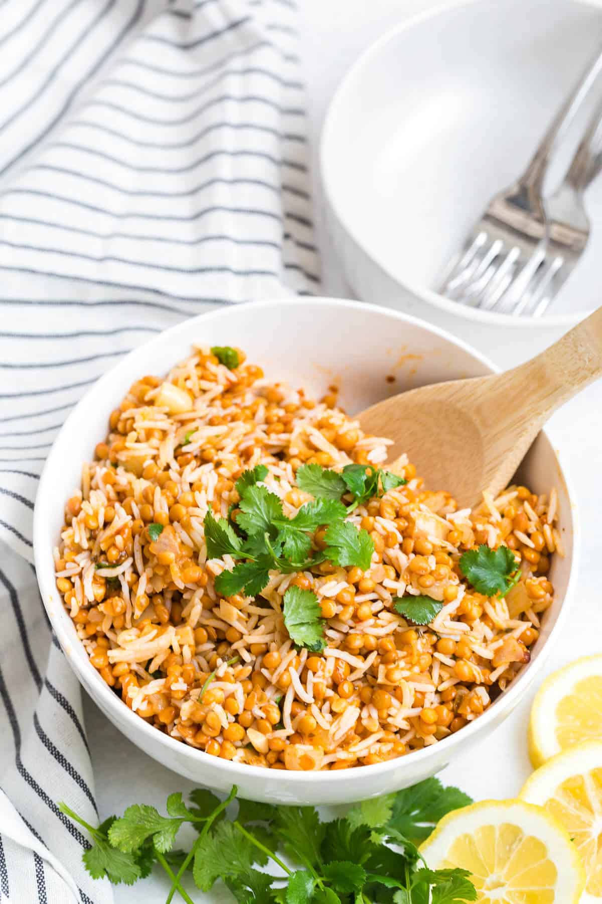 Curried lentil rice in a white bowl with a wooden serving spoon.