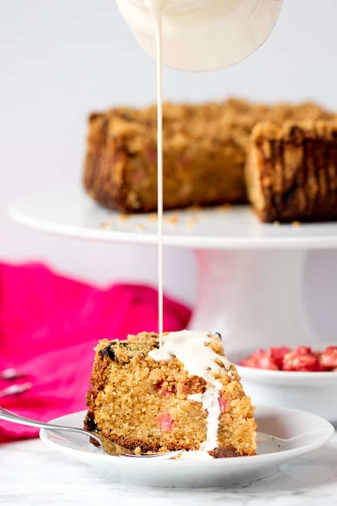 A slice of rhubarb crumble cake with cream being poured on it.