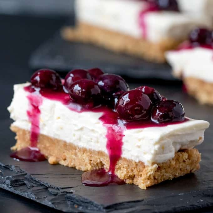 Blueberry and lemon cheesecake bars on a dark surface.