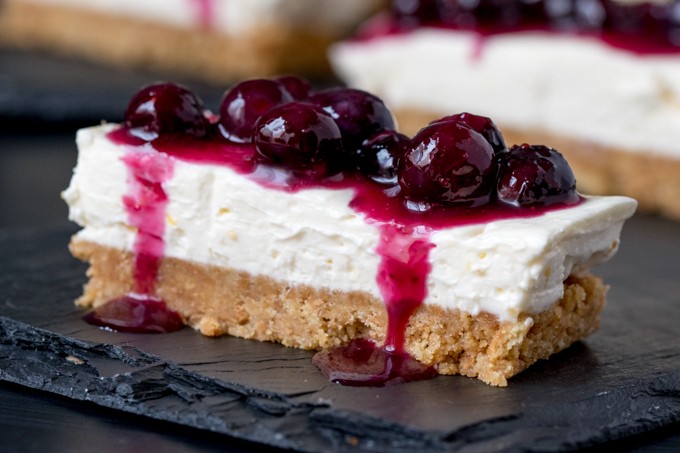 Blueberry and lemon cheesecake bars on a dark surface.