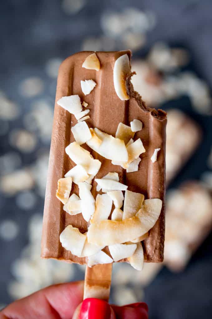 A hand holding a toasted coconut fudgsicle with a bite out of the top.