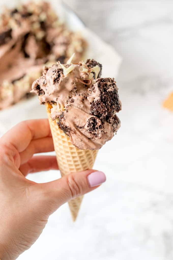 A hand holding a chocolate cake ice cream cone.
