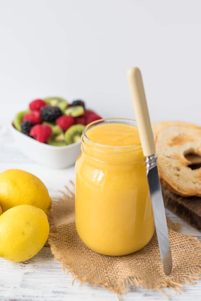 Homemade lemon curd in a glass jar with a butter knife.