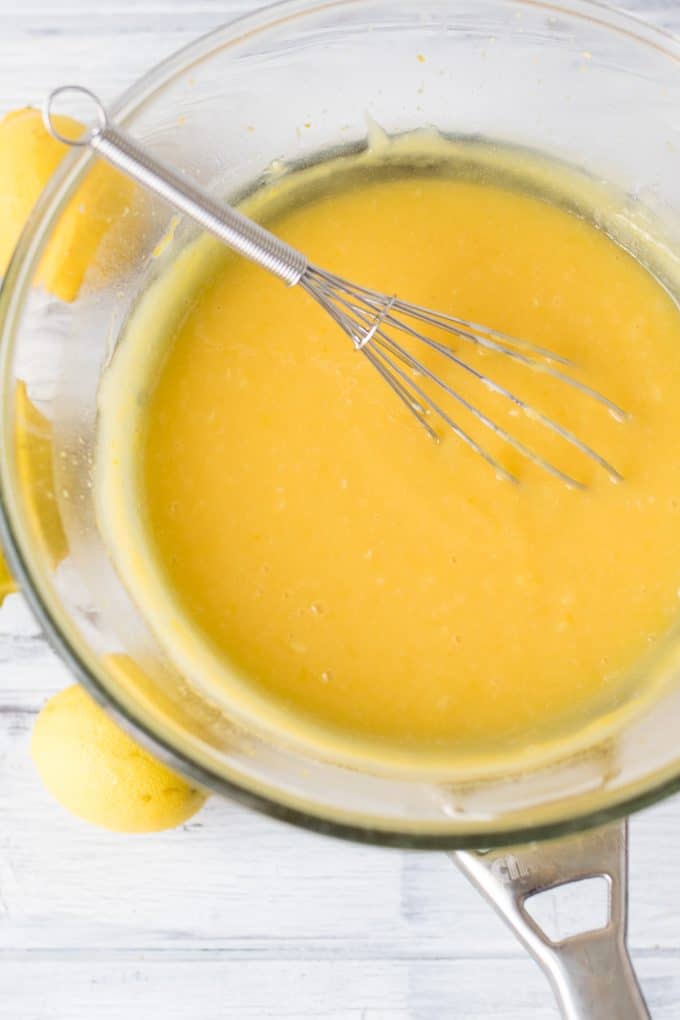 Homemade lemon curd in a glass pot with a whisk.